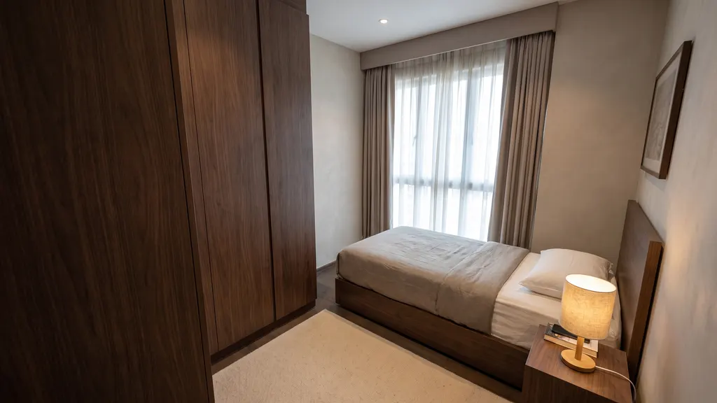 Photoreal render of bedroom 2 in the Ang Mo Kio 4-room HDB sample, Warm Modern Luxe: super single bed in a walnut frame, a bedside lamp, full-height walnut wardrobe and sheer and taupe curtains